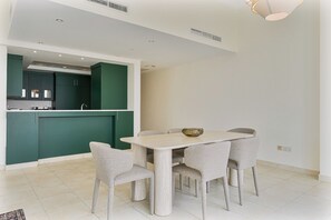 A modern kitchen with green cabinets and a dining area with a light-colored table and chairs. - Stunning 2BR Penthouse | 8-Min to Dubai Marina (Dubai)