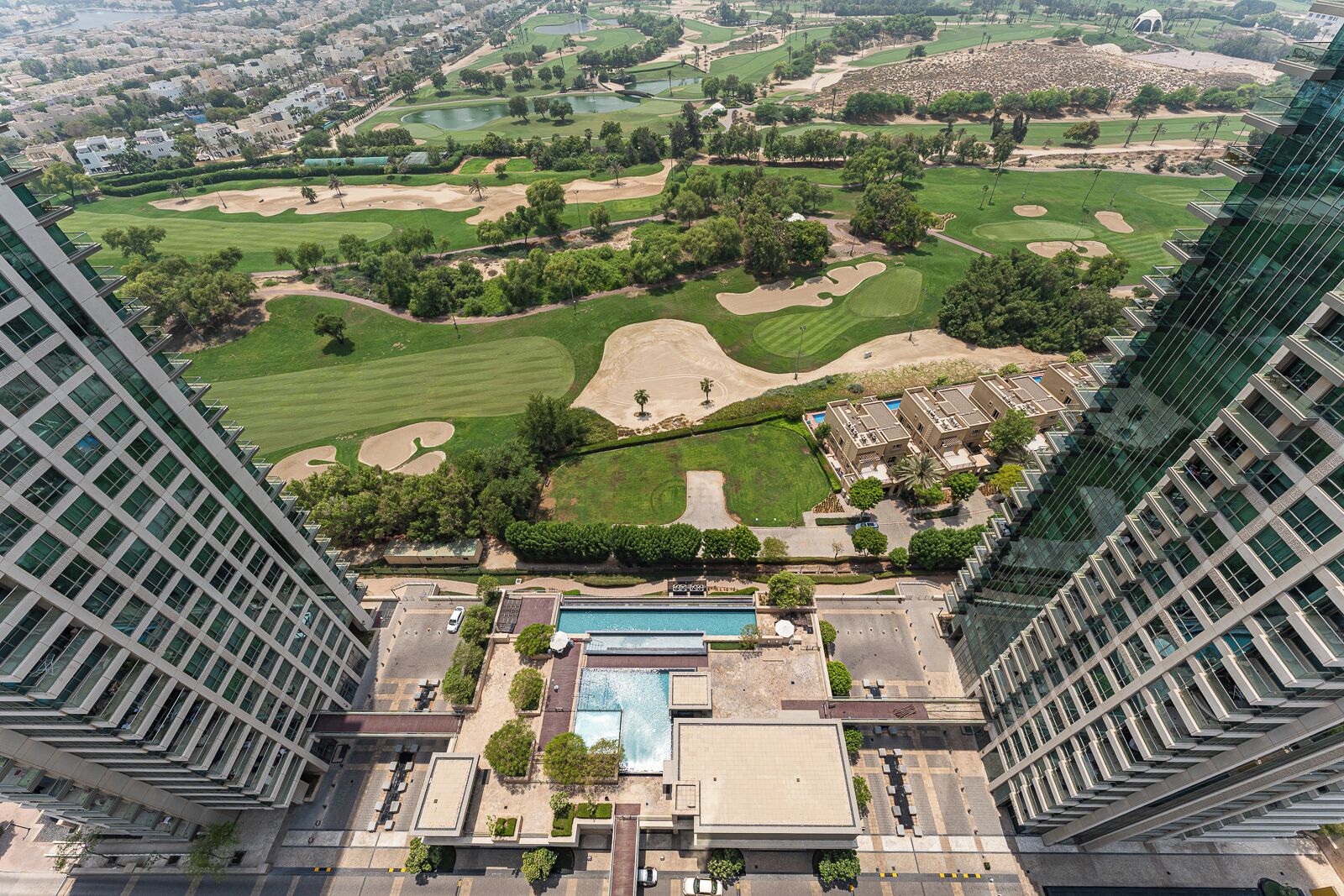 A high-rise hotel overlooking a golf course with a swimming pool and a parking area.