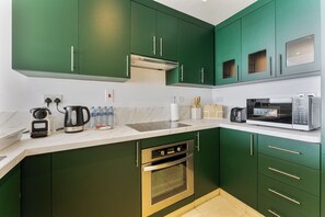 Eine moderne Küche mit grünen Schränken, einem eingebauten Backofen, einer Mikrowelle und einem Wasserkocher.
