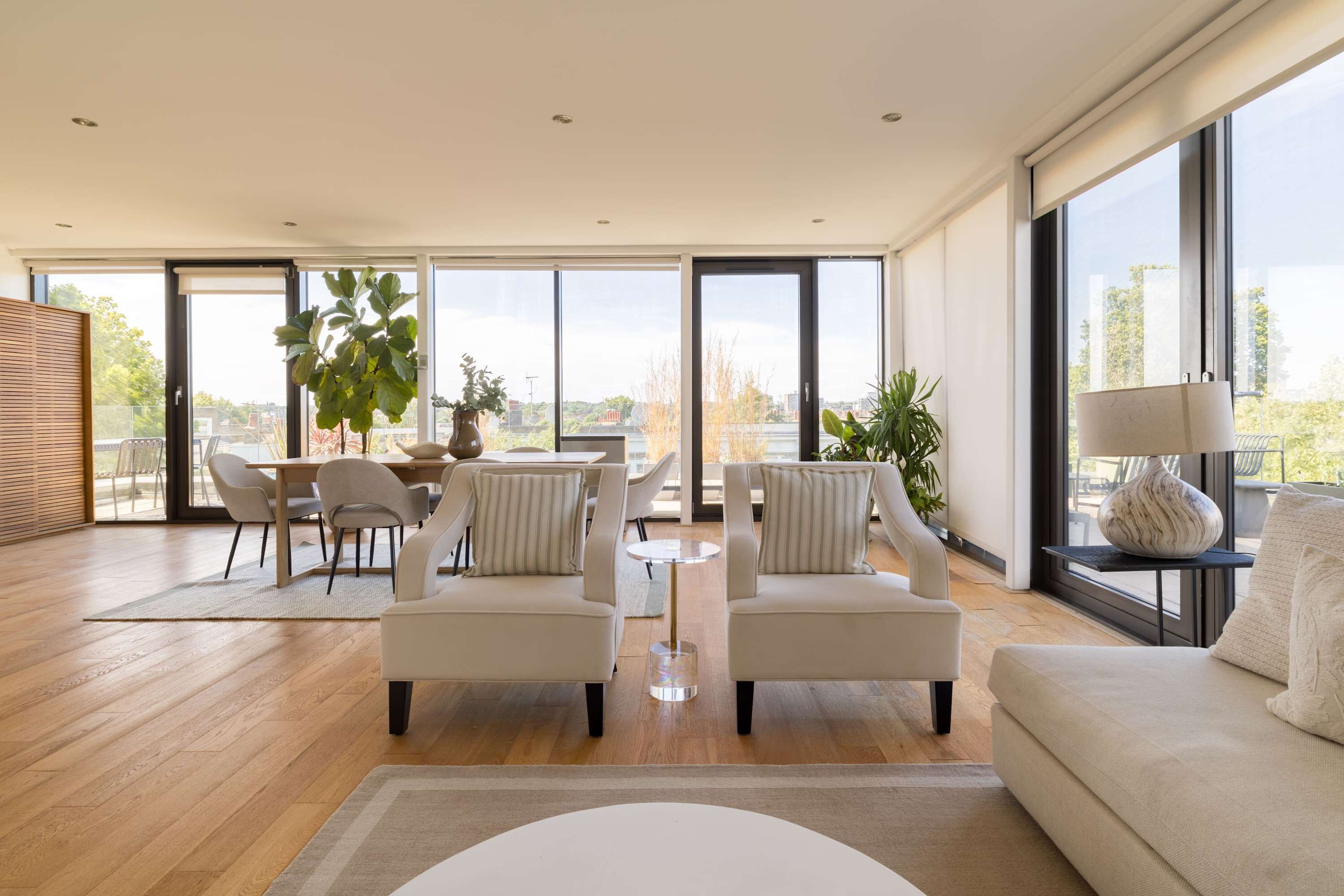 A spacious living room with a large dining area, multiple seating options, and large windows offering views of the outdoors.