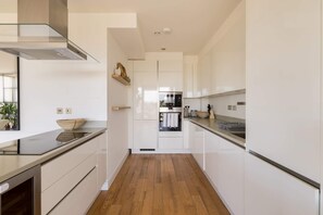 Une cuisine moderne avec des meubles blancs, une hotte en acier inoxydable et un plancher en bois.