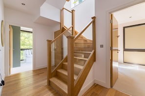 A modern interior with a wooden staircase, a glass door leading outside, and a view of greenery. - Terrace Light in the Vale (Greater London)