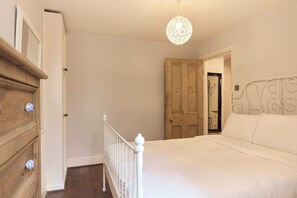 Une chambre à coucher avec un lit, une porte en bois, une commode blanche et un luminaire suspendu.