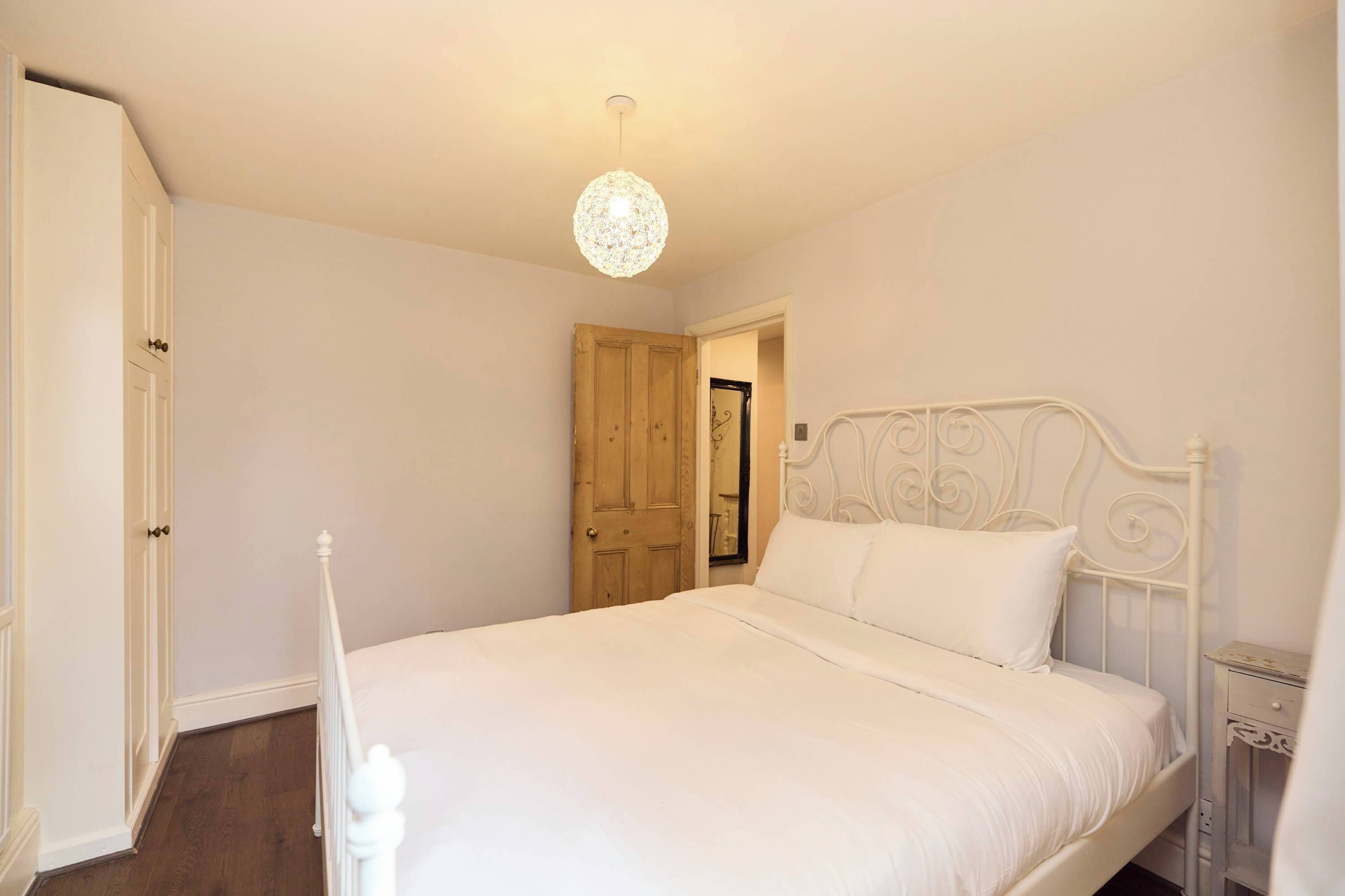 A bedroom with a white bed, a wooden door, and a hanging light fixture.