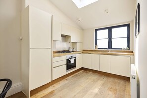 A modern kitchen with white cabinetry, a wooden countertop, a built-in oven, and a window with a black frame. - A Place to Dwell - Tooting (Greater London)