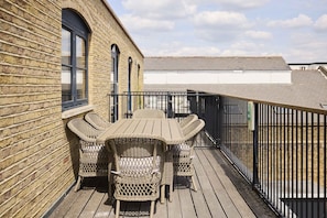 A wooden deck with a table and chairs, a brick wall, and a metal railing. - A Place to Dwell - Tooting (Greater London)
