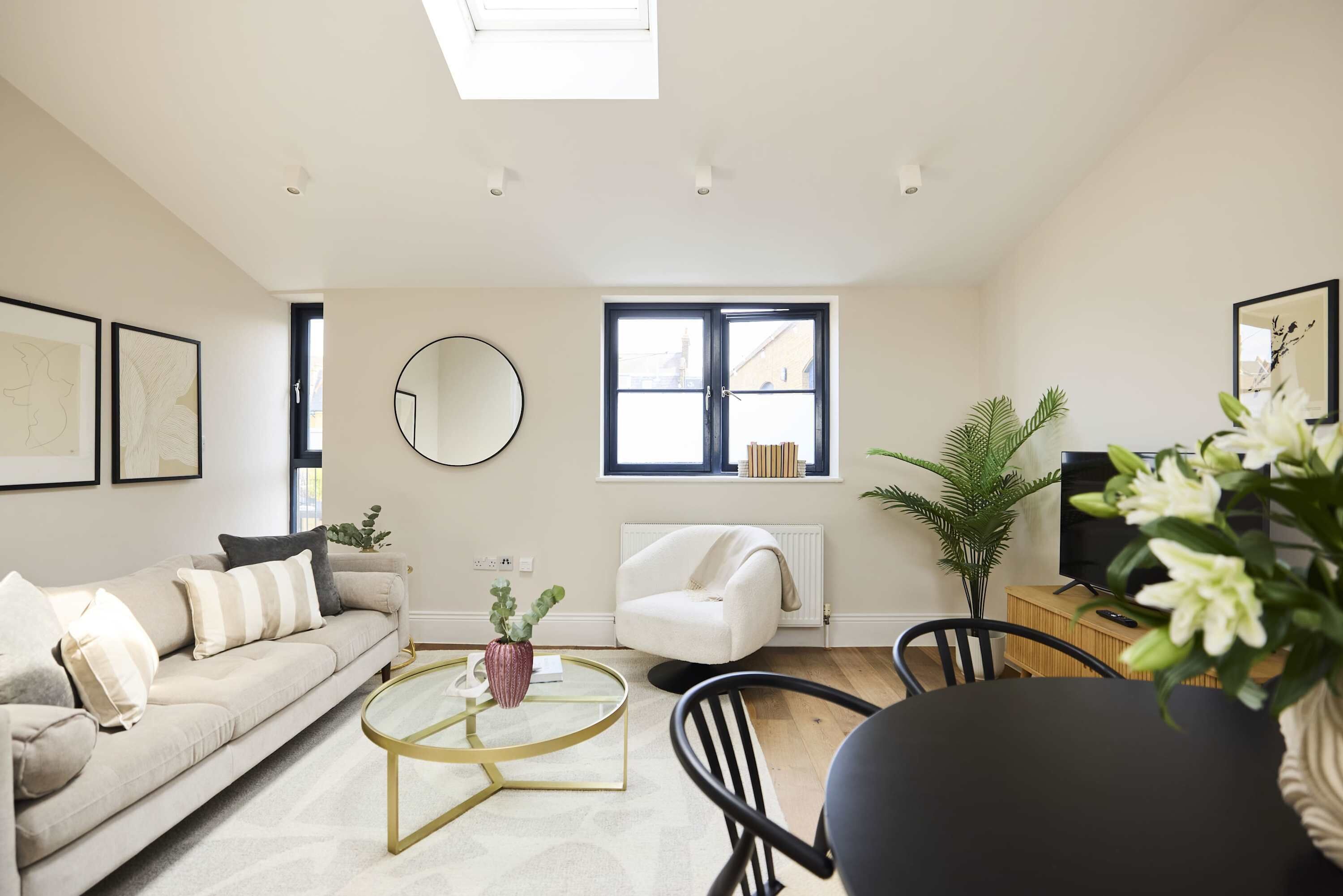 Un salon moderne avec un canapé, une table basse et un fauteuil. On y trouve une fenêtre avec des stores, un radiateur et un téléviseur.
