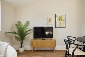 A living room with a flat-screen TV on a wooden cabinet, a potted plant, and two framed artworks on the wall. - A Place to Dwell - Tooting (Greater London)