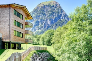 Een modern gebouw met meerdere verdiepingen, grote ramen en een houten terras.