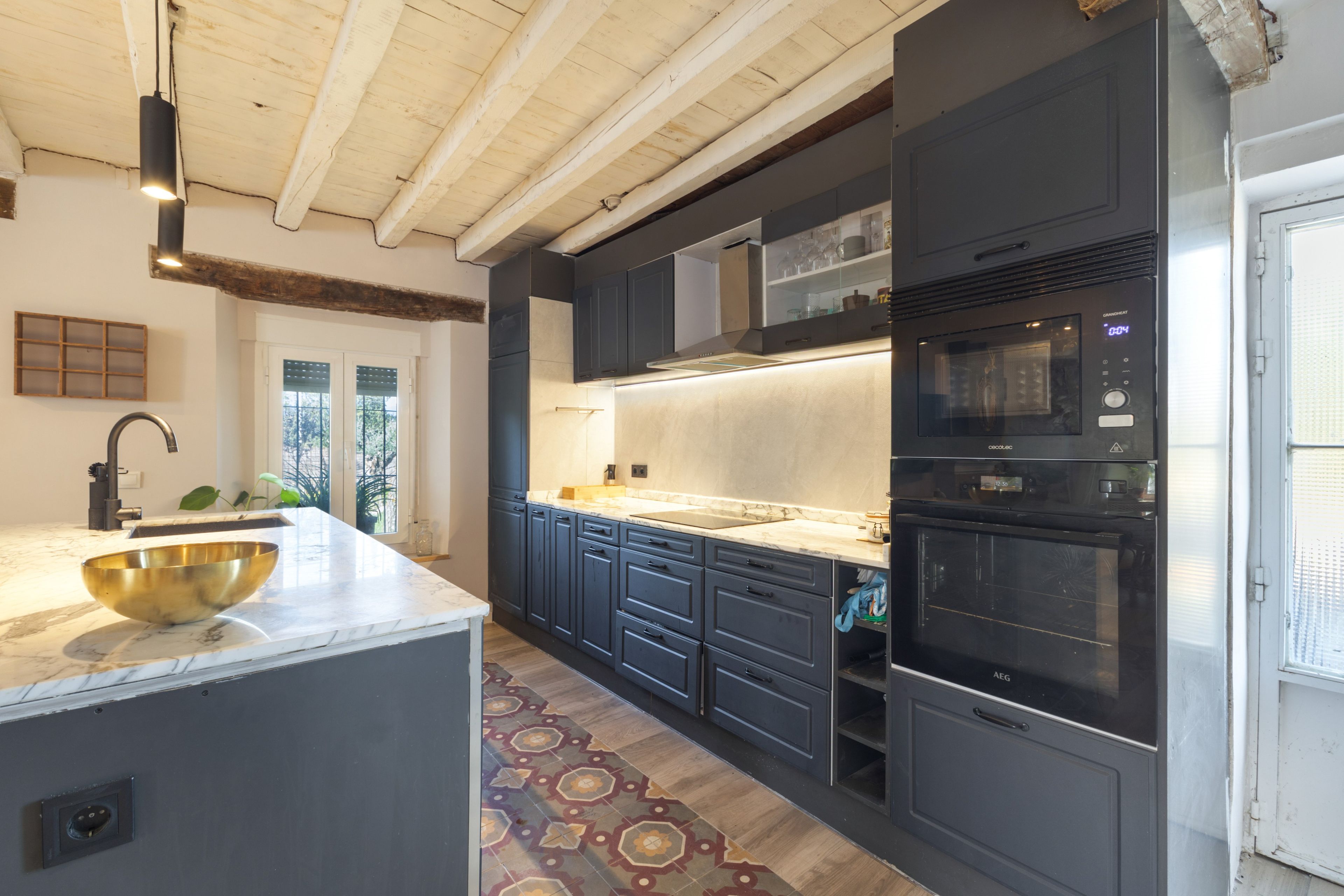 Una cocina moderna con armarios oscuros, encimera de mármol y horno empotrado.