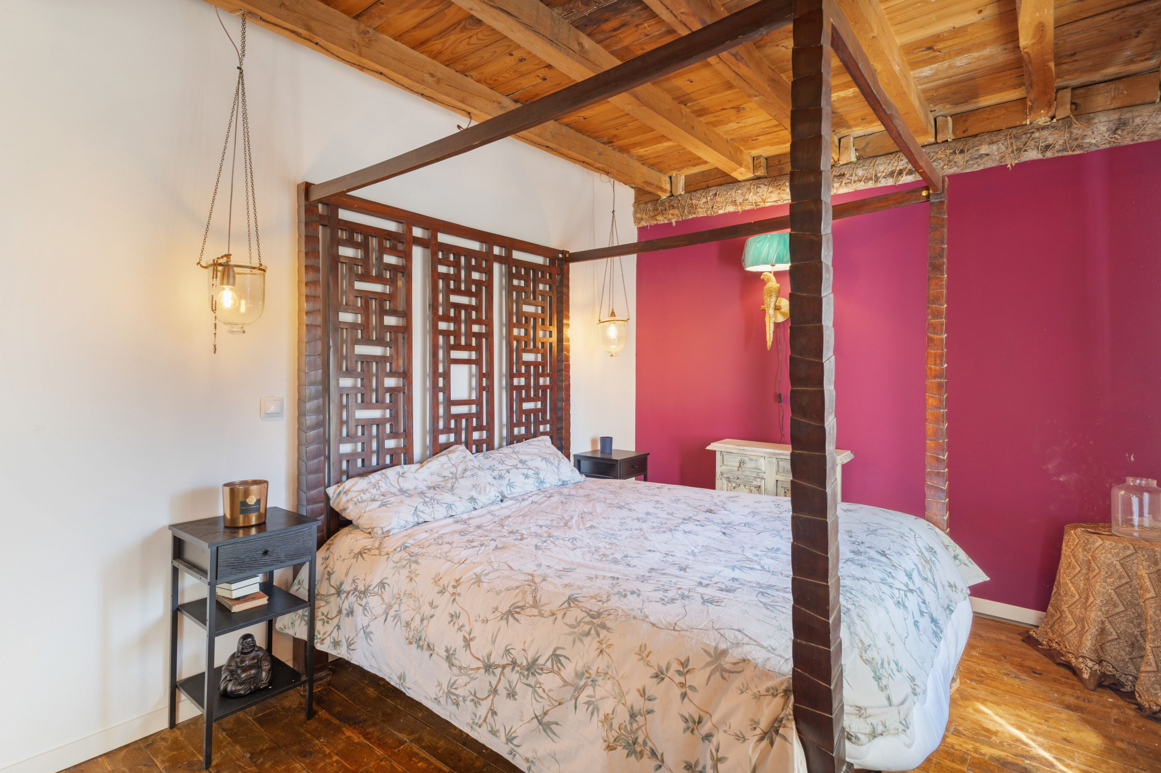 Un lit à baldaquin avec une couvre-lit à motifs floraux, une tête de lit en bois et une table de chevet avec une lampe.