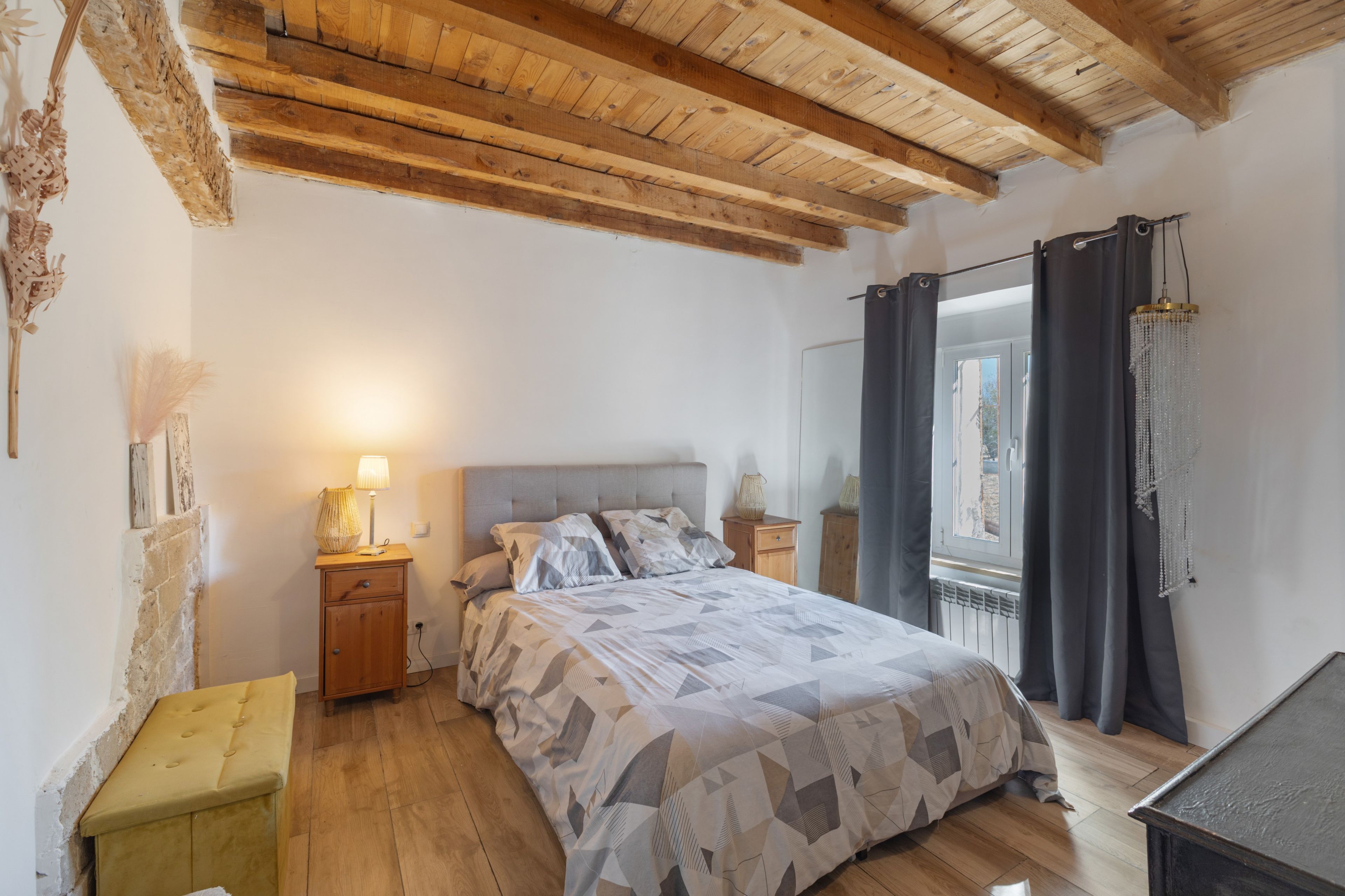 Une chambre à coucher avec un lit, des tables de chevet, une lampe, une fenêtre avec des rideaux et un plafond en bois.