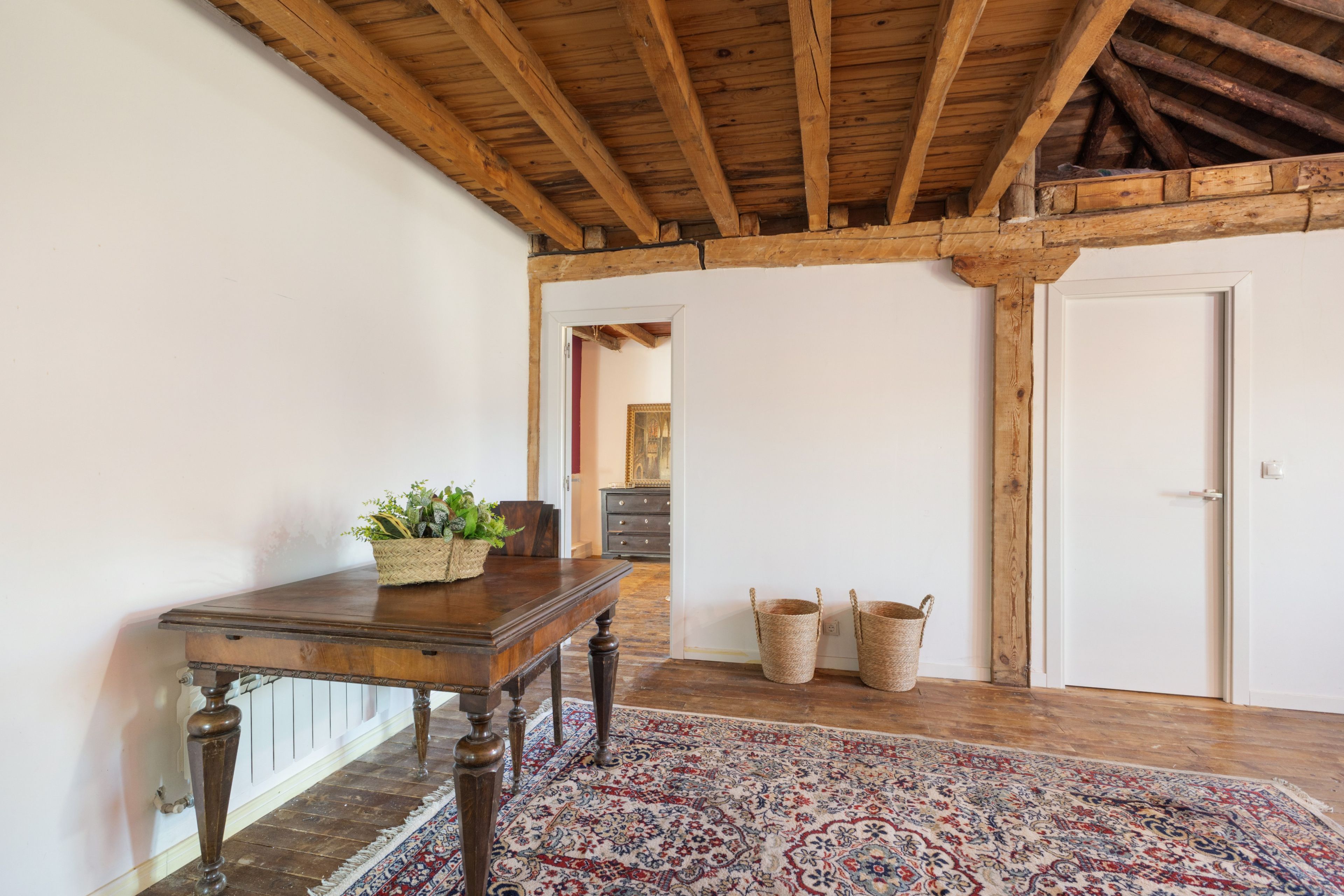 A room with a wooden table, a patterned rug, and a wooden ceiling.