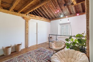 A rustic room with exposed wooden beams, a white door, a hanging chair, a patterned rug, and a potted plant.
