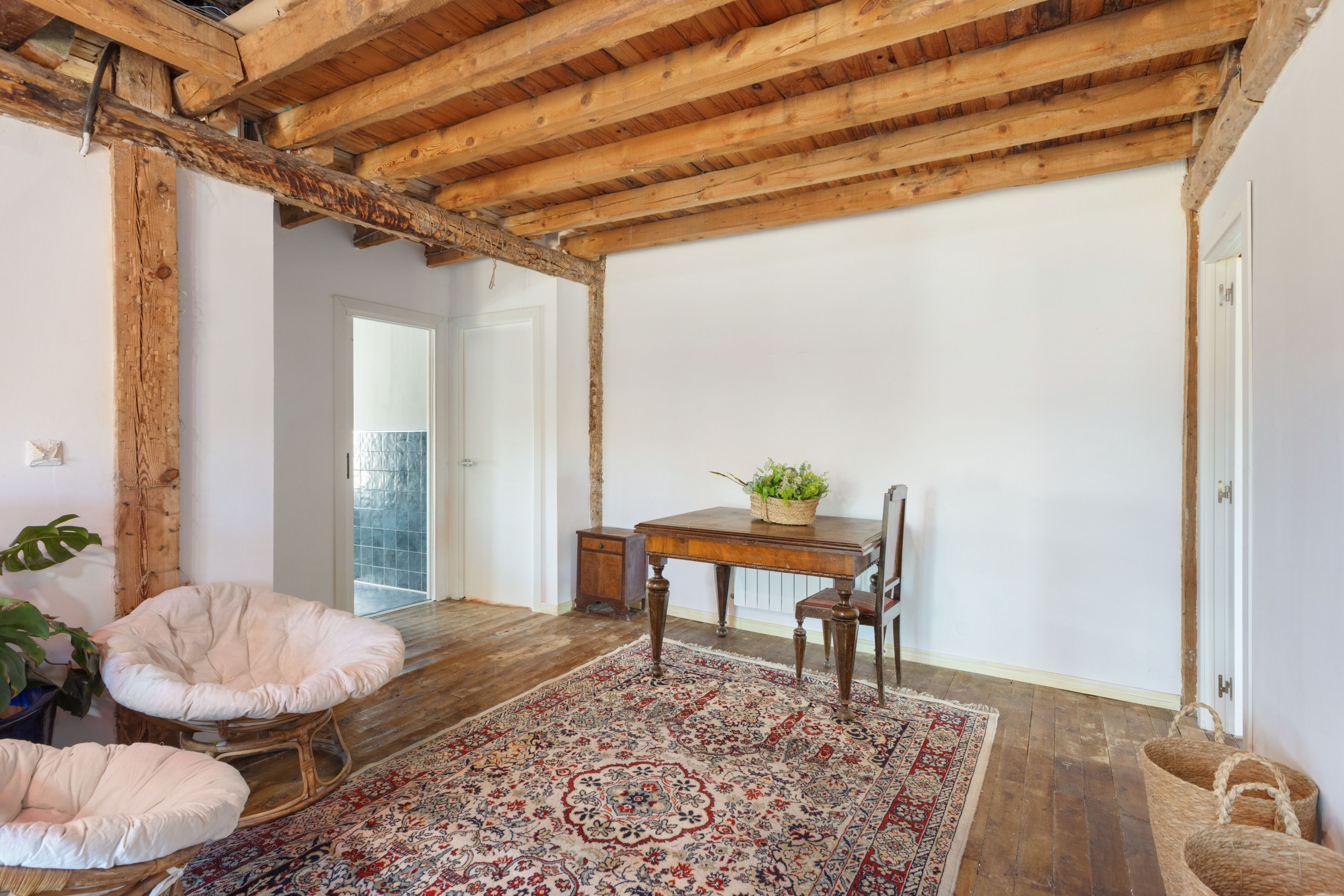 Una habitación con techo de madera, una mesa de comedor con sillas, un tapete estampado y una planta en maceta.