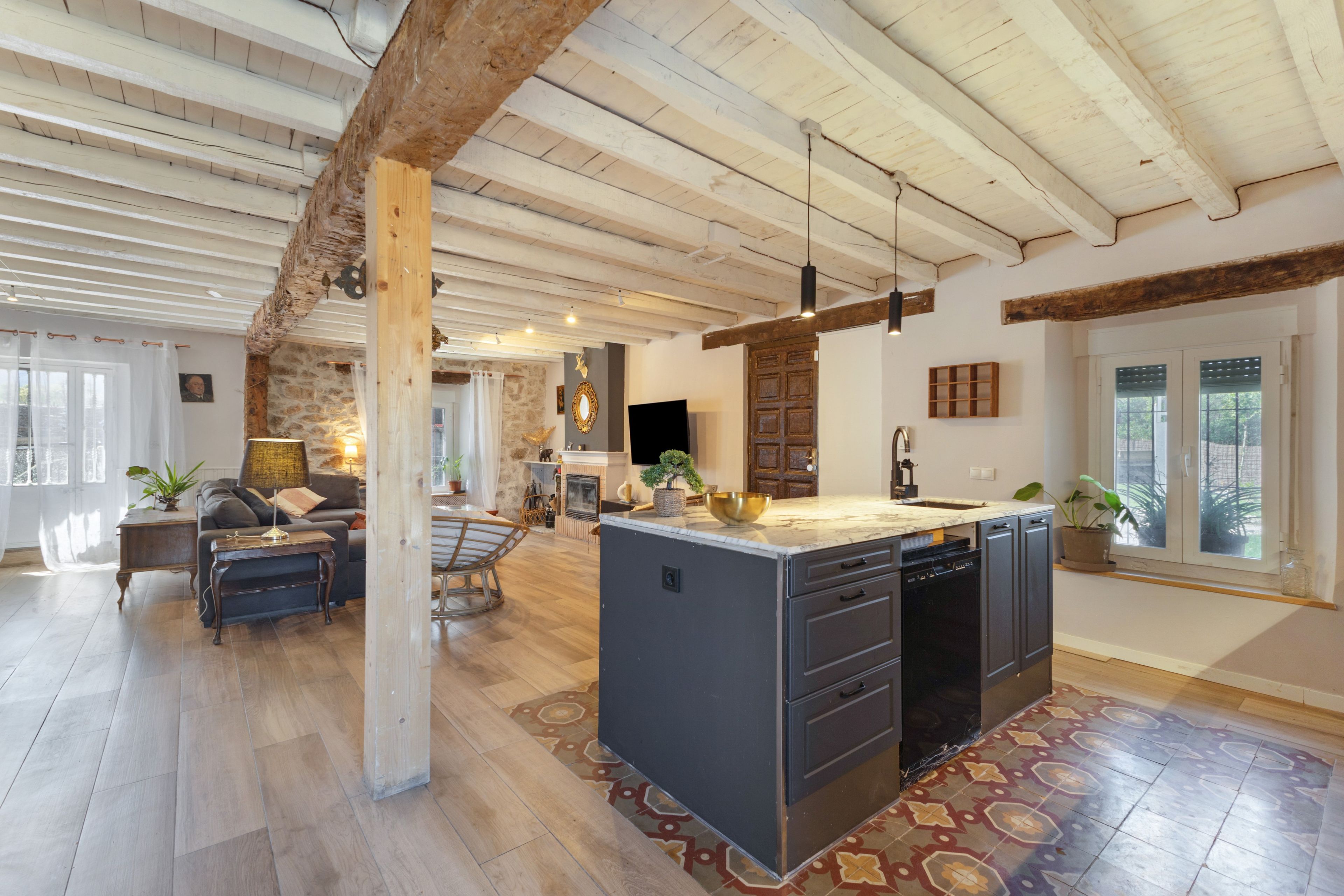 A spacious living area with a large island, wooden beams on the ceiling, and a stone wall.