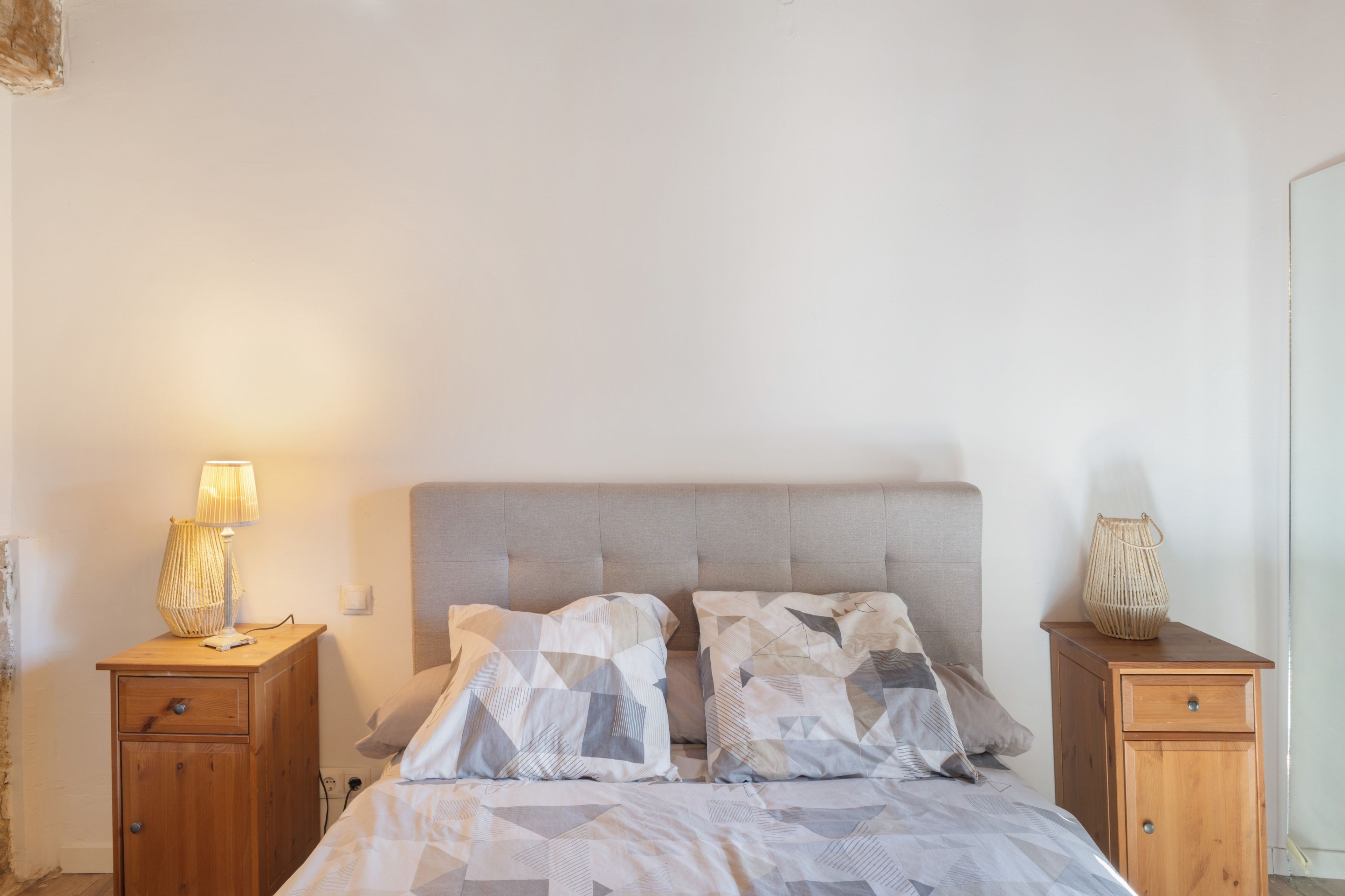 Een slaapkamer met een bed, twee nachtkastjes, een lamp en een geweven mand.
