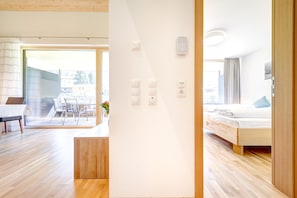 A modern hotel room with a wooden floor, a bed with a headboard, a desk with a chair, and a view of the outside. - Ferienwohnung Motta Lodge (Brand)