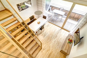 A modern interior with a wooden staircase, a dining area with a white table, and a view of an outdoor patio. - Ferienwohnung Motta Lodge (Brand)