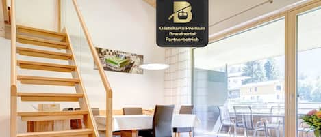 A modern interior with a wooden staircase, a dining area, and a view through a glass door.