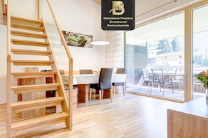 A modern interior with a wooden staircase, a dining area, and a view through a glass door. - Ferienwohnung Motta Lodge (Brand)