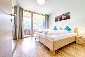 A hotel room with a wooden bed, a nightstand, a window with curtains, and a painting on the wall. - Ferienwohnung Motta Lodge (Brand)