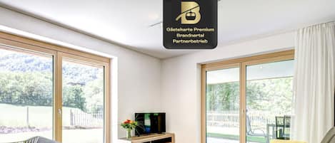 Una sala de estar moderna con un sofá, una mesa de centro y un televisor. Amplios ventanales correderos dan acceso a un espacio exterior.