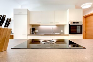 A modern kitchen with a built-in induction cooktop, a coffee maker, and a stainless steel oven. - Gartenferienwohnung Alvier Lodge (Brand)