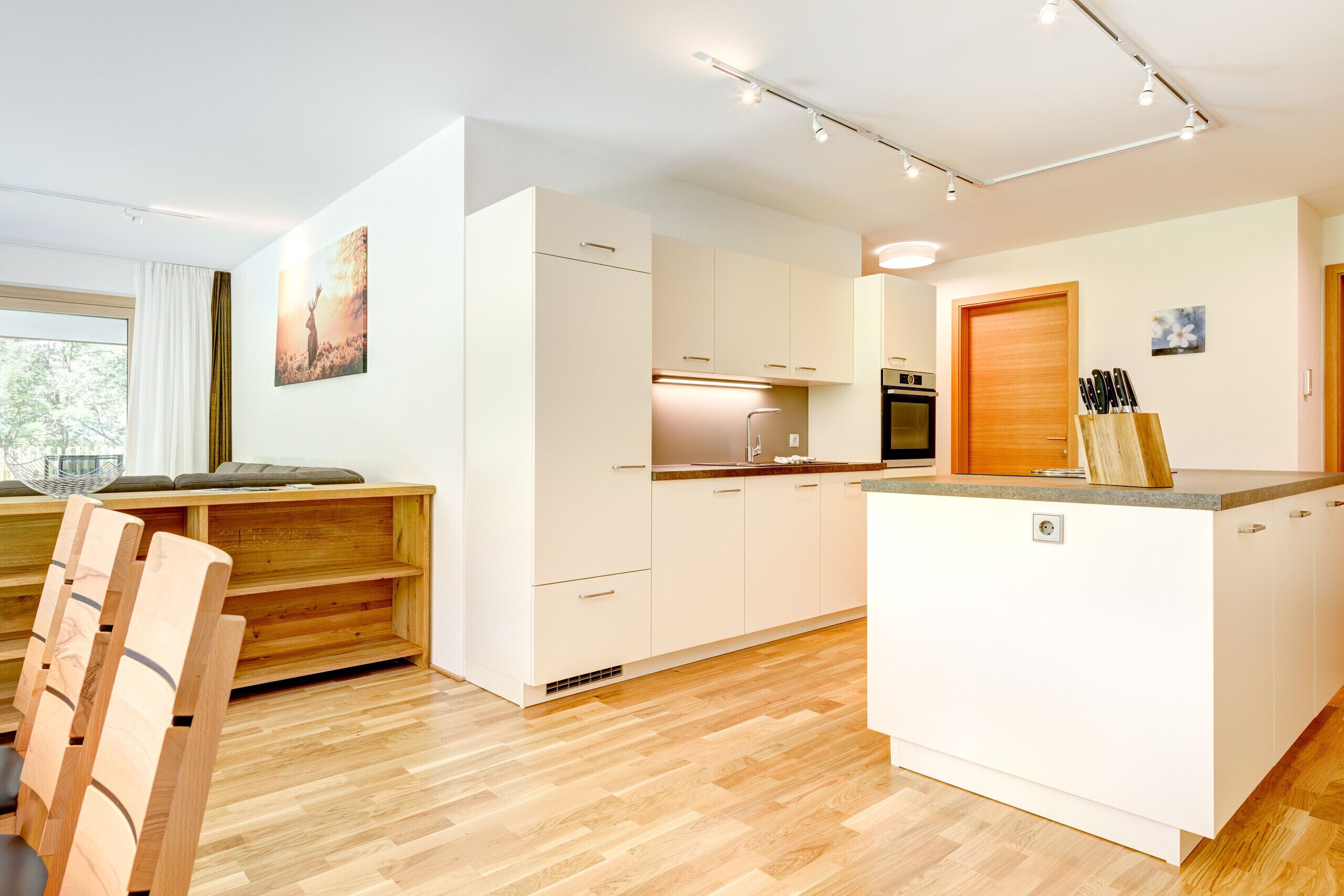 A modern kitchen with white cabinetry, a wooden dining table, and a large window.