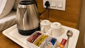 Habitación de hotel con cama, mesita de noche con tetera, dos tazas, bandeja con paquetes de comida y una cuchara.