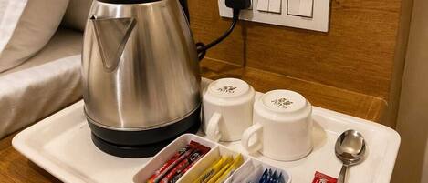 Une chambre d’hôtel comprenant un lit, une table de chevet avec une bouilloire, deux tasses, un plateau avec des portions de nourriture emballées et une cuillère.