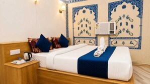 Una habitación de hotel con cama, una mesita de noche con hervidor, una bandeja con tazas y una alfombra roja.