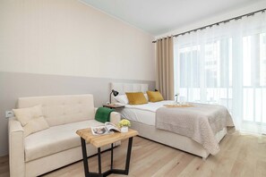 Una habitación de hotel con cama, sofá, una mesita y ventana con cortinas.