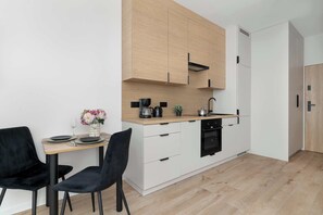 Cocina moderna con armarios blancos, encimera de madera y una zona de comedor con dos sillas negras y una mesa pequeña.