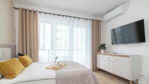 Ein modernes Schlafzimmer mit Bett, Nachttisch, Fernseher und einem Fenster mit Vorhängen.