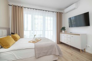 Ein modernes Schlafzimmer mit Bett, Nachttisch, Fernseher und einem Fenster mit Vorhängen.