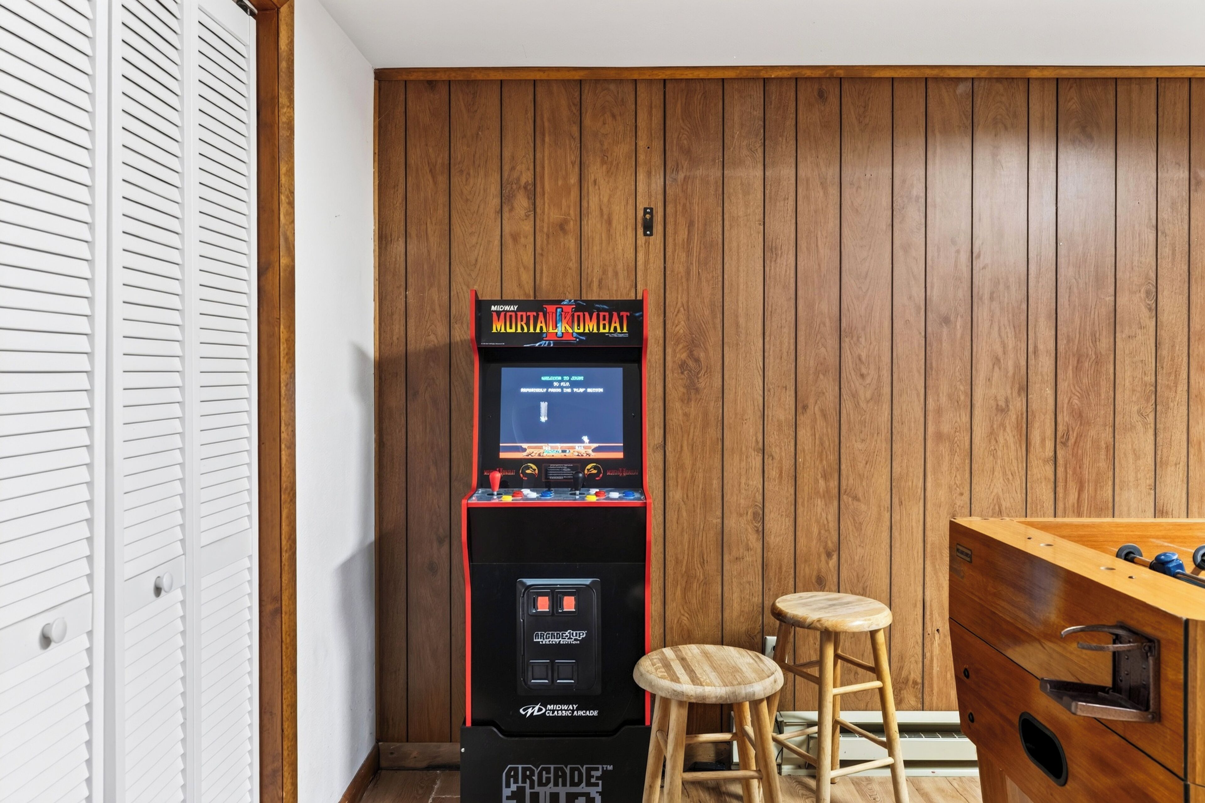 Ein Midway-Spielautomat in einem Raum mit Holzwandverkleidung und einem Tischfußballspiel.