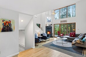 Un salon spacieux doté d’une cheminée, d’un escalier et de grandes fenêtres offrant une vue sur l’extérieur.