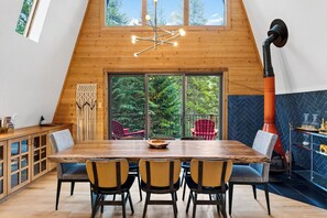 Un espace repas avec une table en bois, des chaises et une vue sur l’extérieur grâce à de grandes fenêtres.