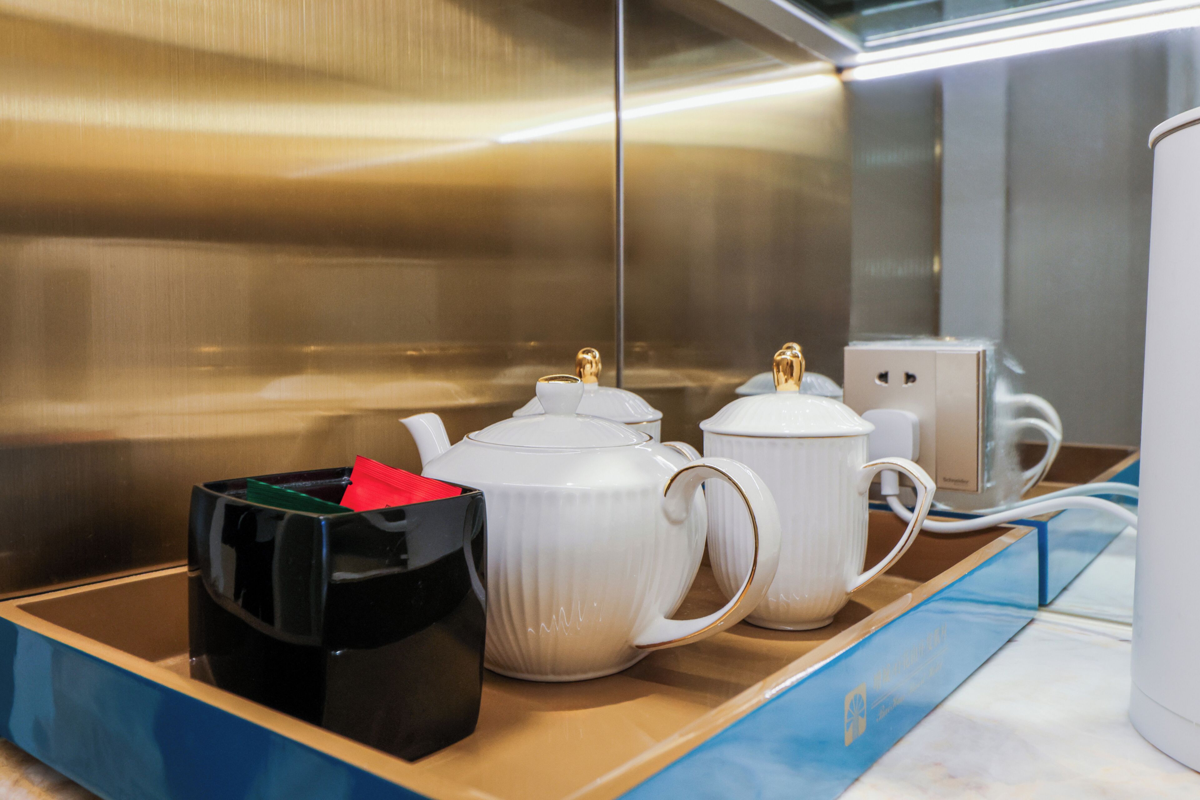 Una encimera de cocina con teteras blancas, un recipiente negro y una taza blanca.