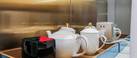 Una encimera de cocina con teteras blancas, un recipiente negro y una taza blanca.