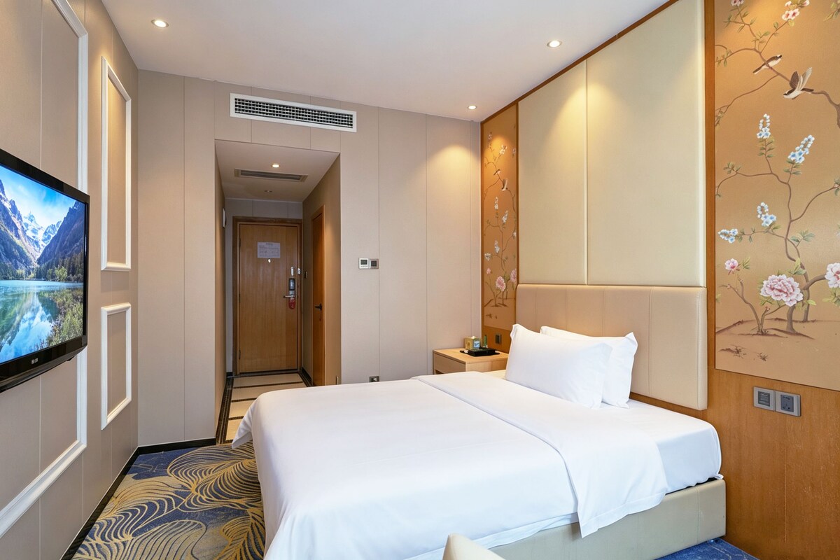 A hotel room with a bed, a television, a nightstand, and a wall with a floral design.