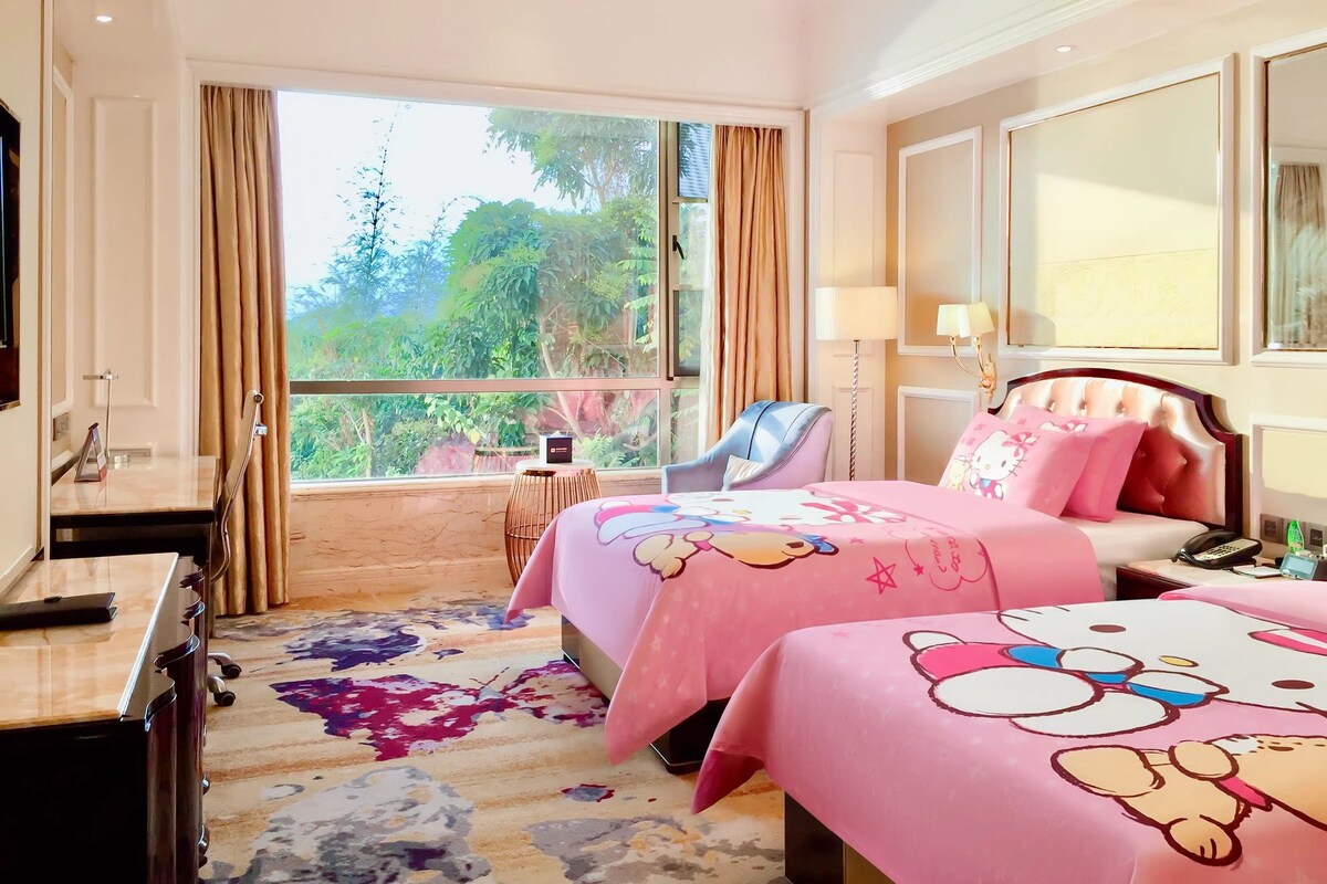 A hotel room with a large window, a bed with pink bedding, a bedside table, a chair, and a desk with a lamp.