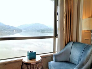A room with a view of a lake and mountains, a blue sofa, a small round table with a box, and a lamp. - Baihua Resort Hotel (Guangzhou)
