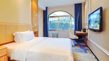 A hotel room with a large bed, a desk, a television, and a view of the outdoors.