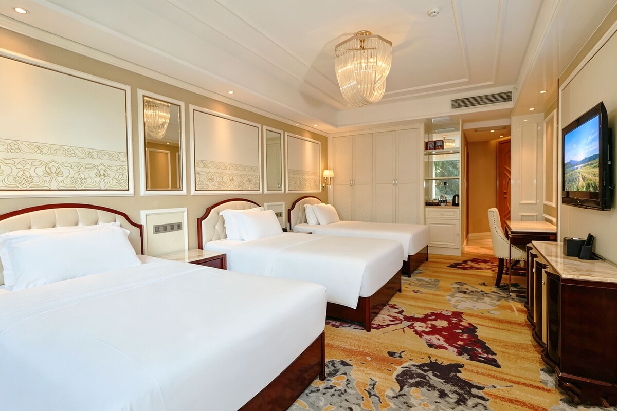 A hotel room with three beds, a television, a desk, and a chandelier.
