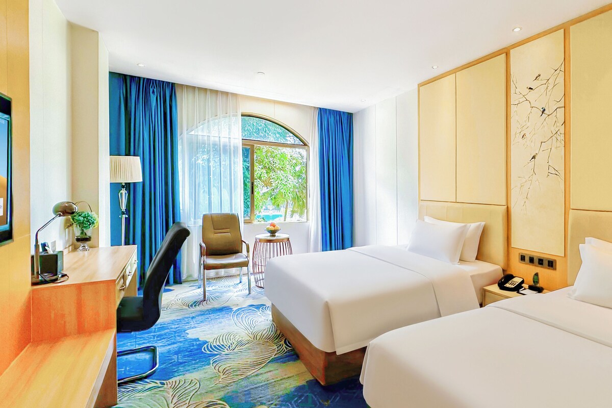 Une chambre d’hôtel avec deux lits, un bureau, une chaise, une petite table et une fenêtre avec des rideaux.