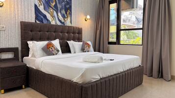 A bedroom with a large bed, a nightstand, a wall-mounted lamp, and a window with curtains.
