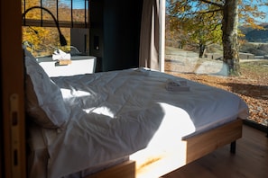 A bedroom with a bed, a bedside table, and a view of the outdoors. - Infinity 4p in Vama Buz Ului (Vama Buzăului)