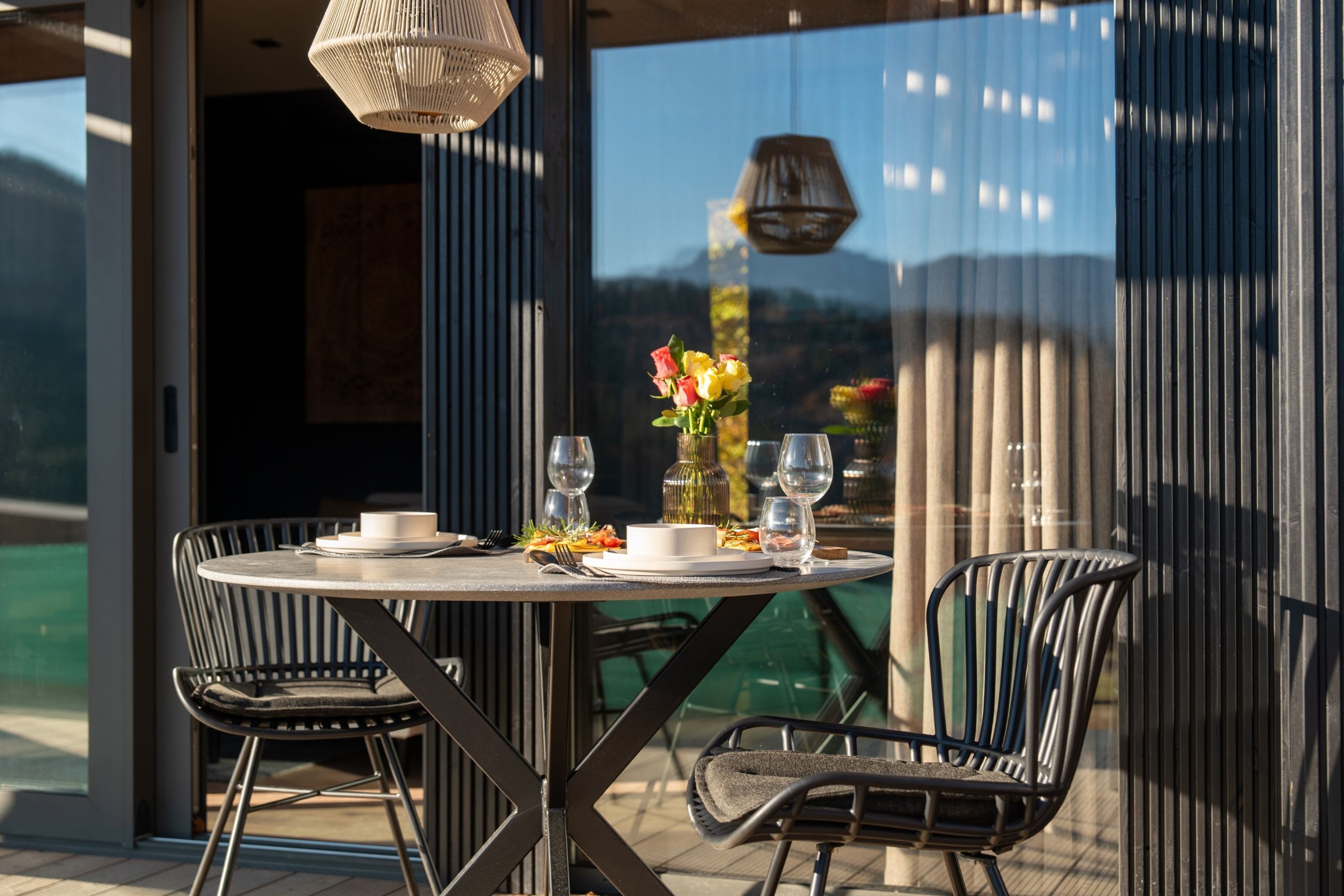 Een terras met een ronde tafel, twee stoelen en een bloevas.